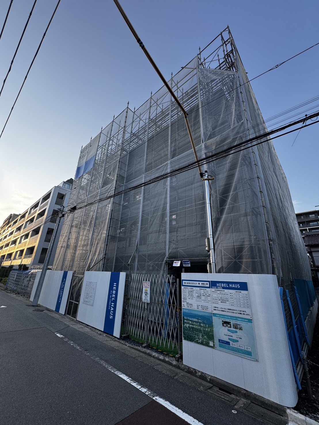 足場とシートに覆われた建築中のマンションを道路から見た様子
