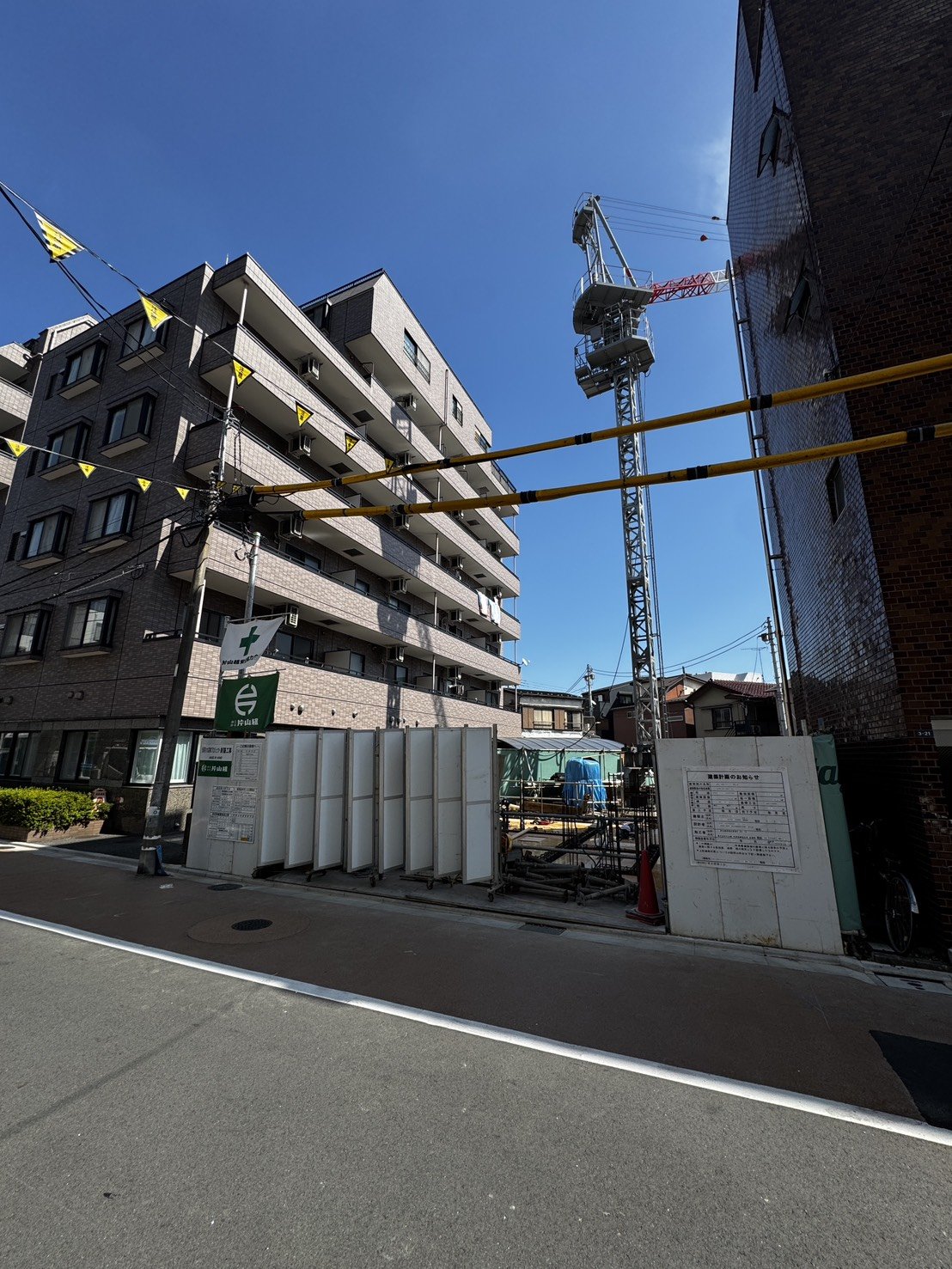 道路越しに見える周辺マンションと建設中のタワークレーン