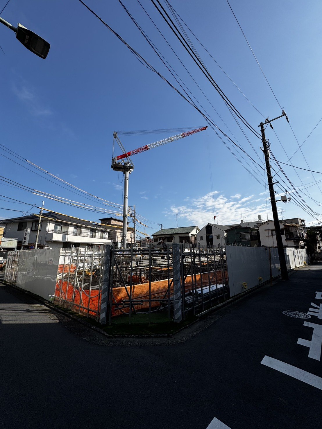 現場を囲む仮囲いとタワークレーン、周辺の住宅街の様子