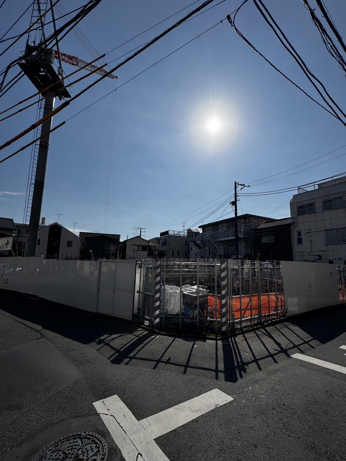 現場上空のタワークレーンと青空、周辺の住宅街